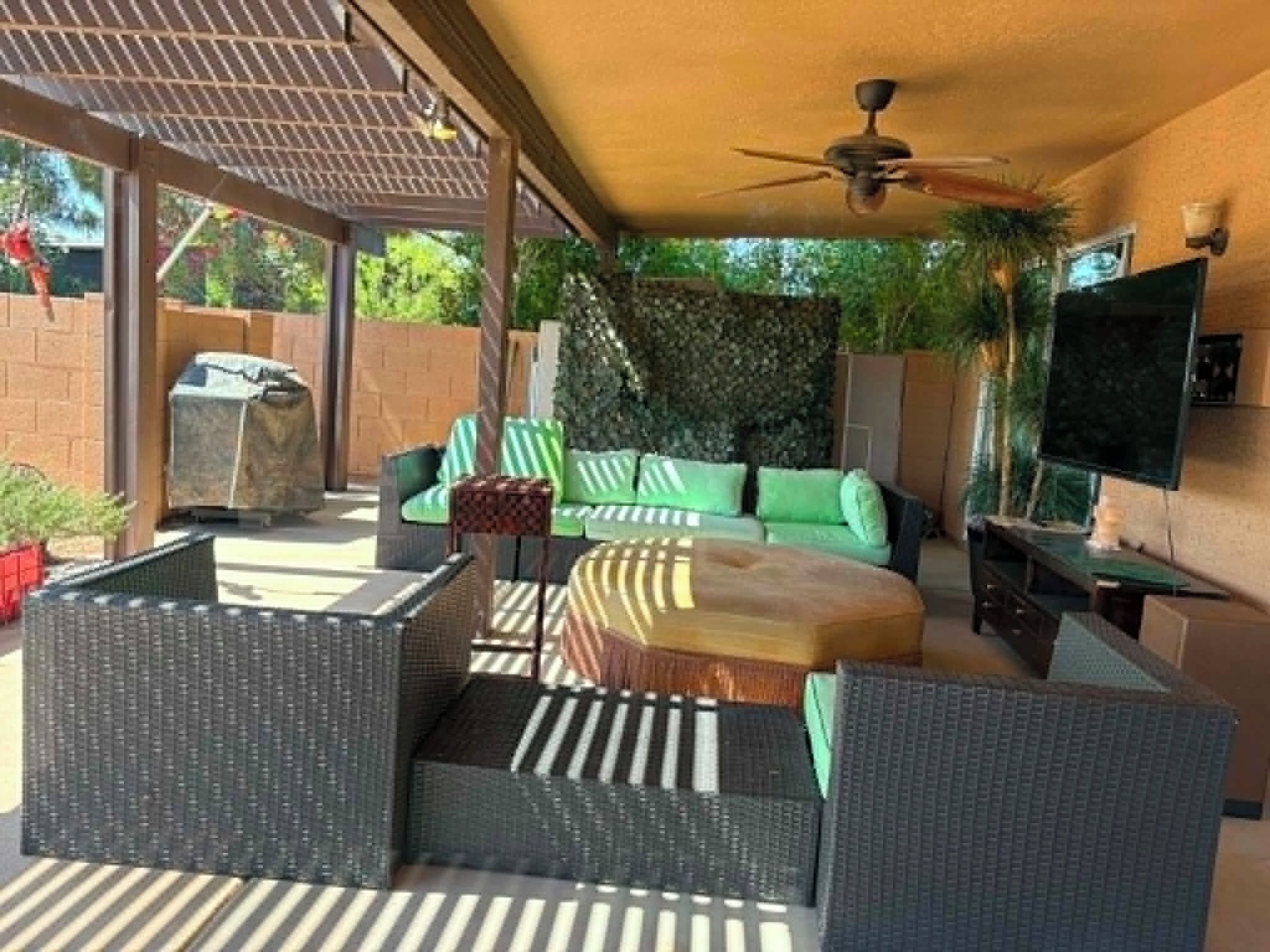An outdoor patio with wicker furniture, a ceiling fan, a TV, and a barbecue grill.