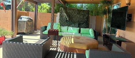 An outdoor patio with wicker furniture, a ceiling fan, a TV, and a barbecue grill.