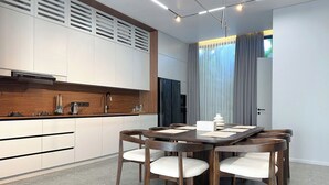 Una cocina moderna con gabinetes blancos, una encimera de madera y un comedor con mesa y sillas de madera oscura.