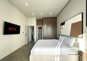 A modern hotel room with a large bed, a flat-screen TV mounted on the wall, and a door leading to a bathroom. - Modern 2BR Villa Umalas Great Location (Umalas)