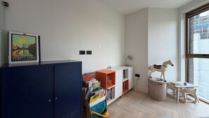 Ein Zimmer mit großem Fenster, einem Bücherregal, einem Schrank und einem kleinen Tisch mit einer dekorativen Pferdefigur.