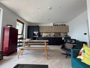 A modern kitchen with wooden cabinets and a dining area with a wooden table and chairs. - Stylish Canal Side 2BDR Flat with Private Balcony (Greater London)