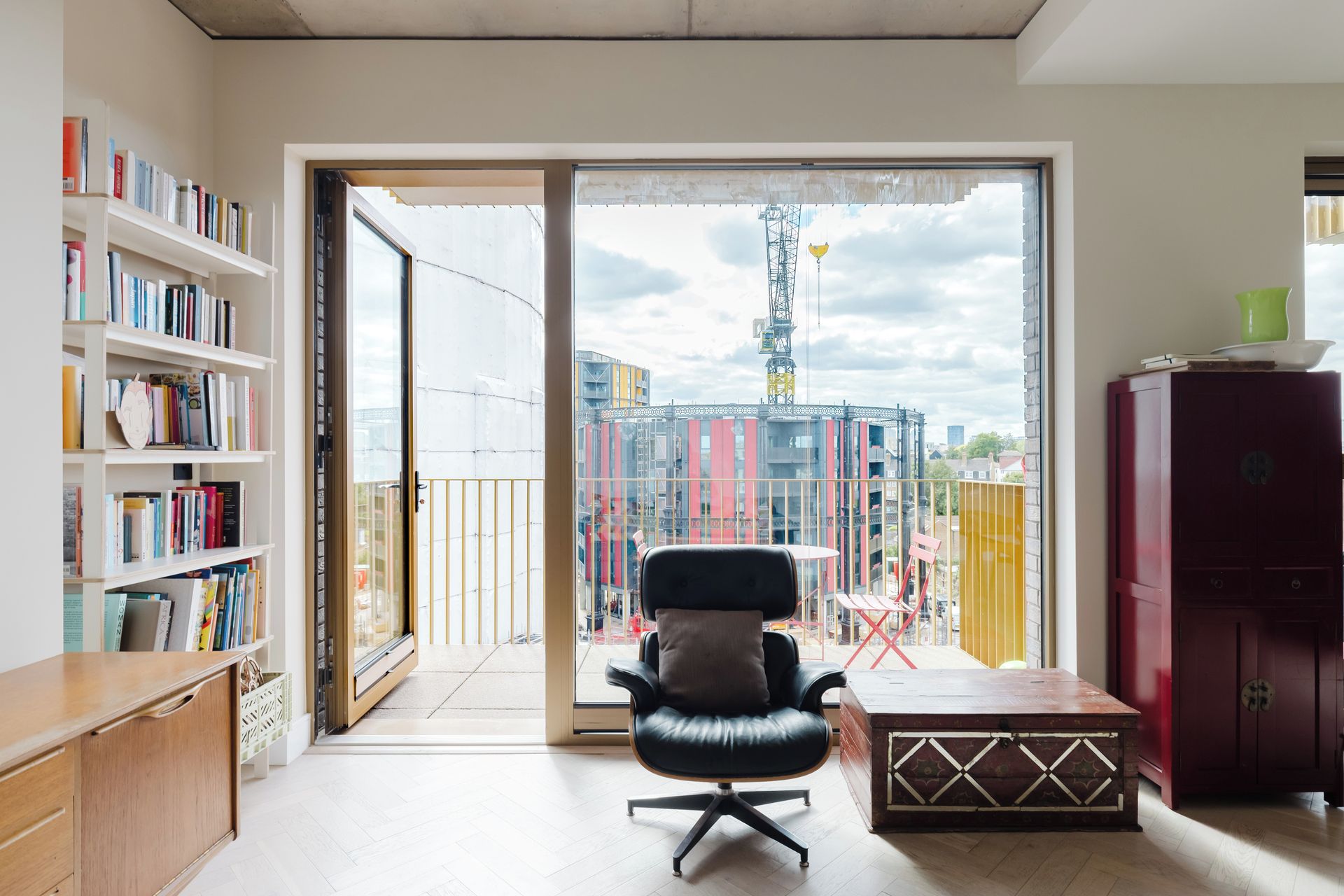 A modern room with a large sliding glass door leading to an outdoor balcony, a black office chair, a wooden desk, and a bookshelf filled with books.