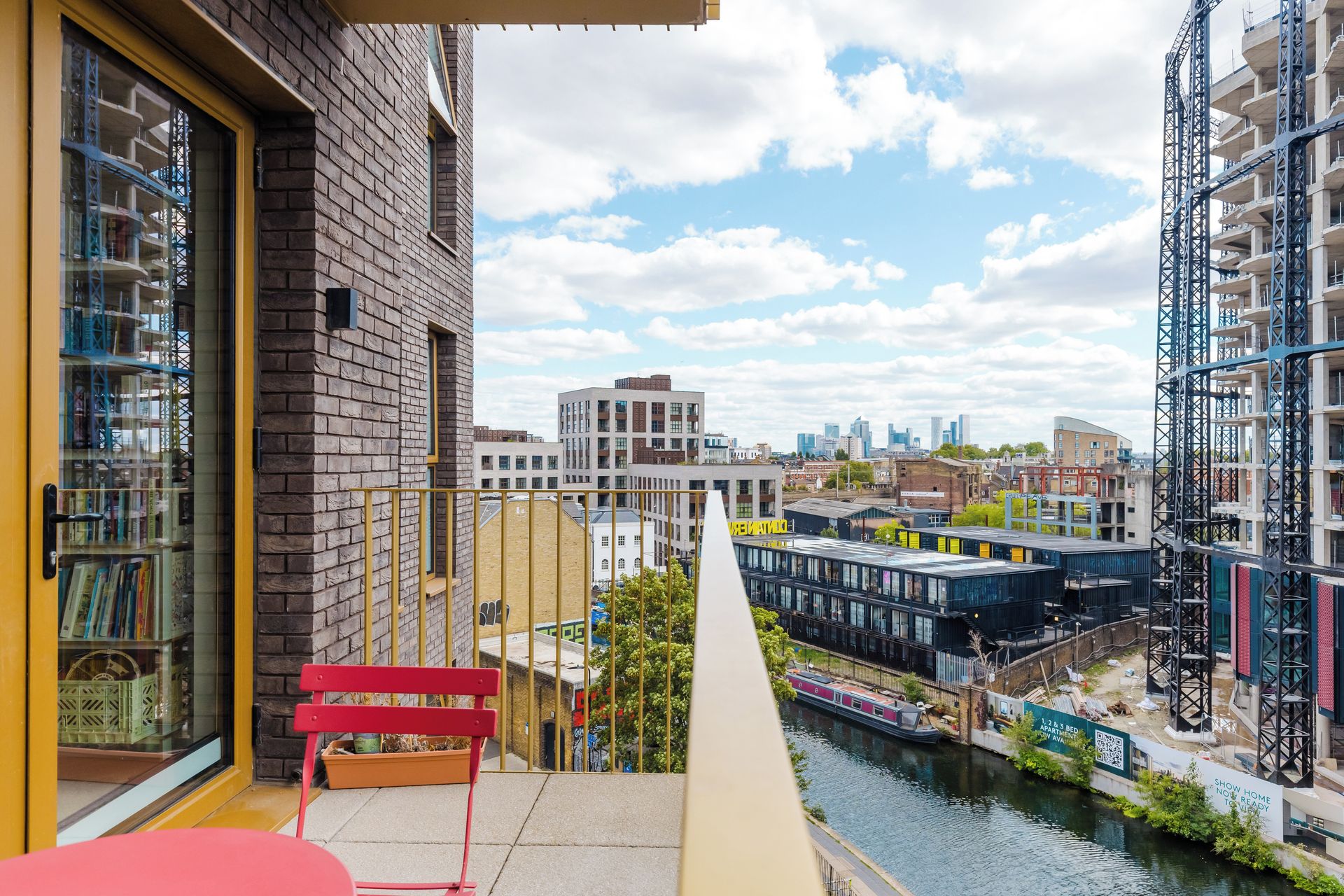 Un balcon donnant sur une rivière, un banc rouge et un bâtiment à la façade en briques.