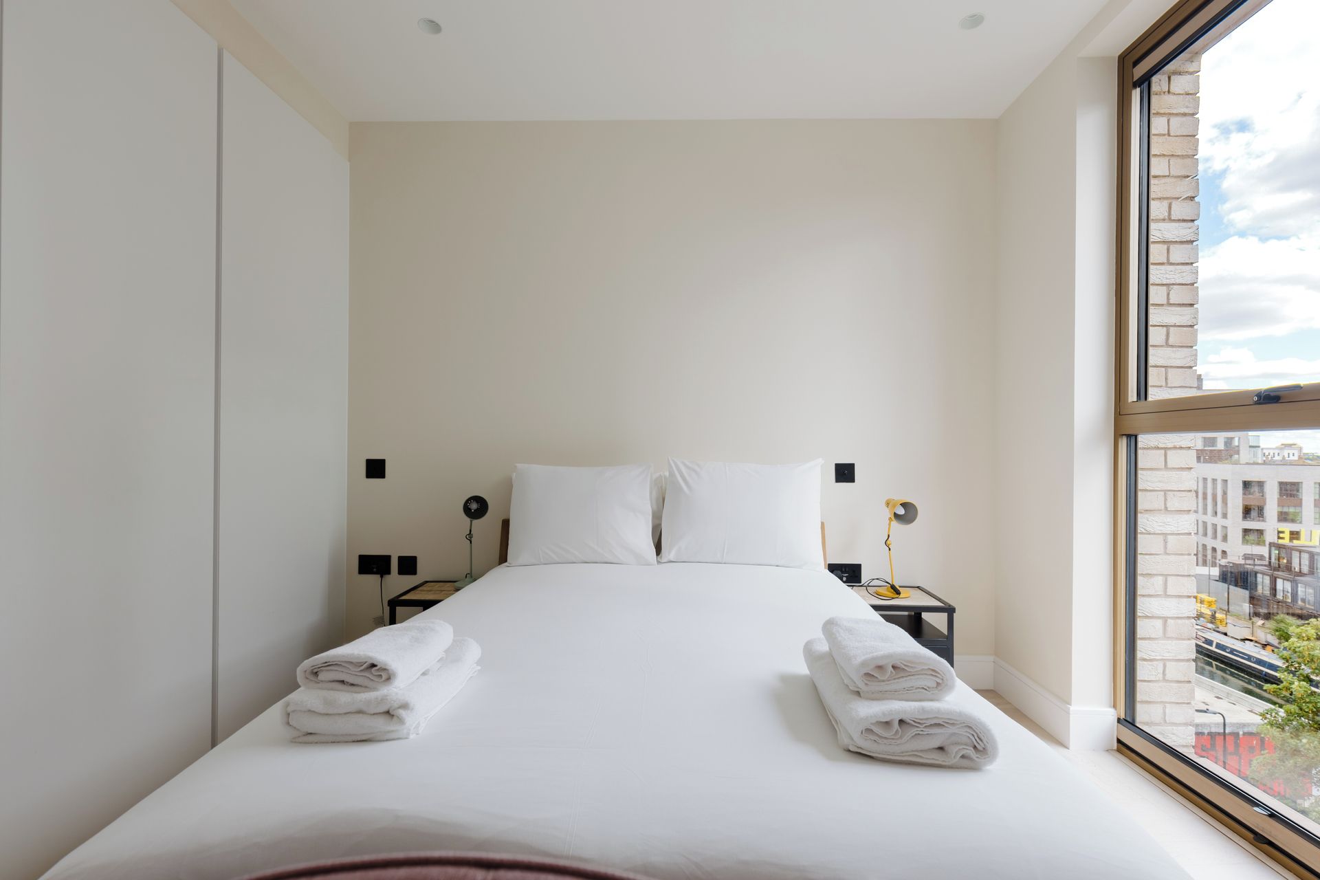 A hotel room with a large bed, two bedside tables, and a view of the city through a window.