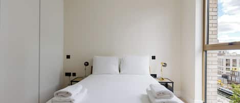 A hotel room with a large bed, two bedside tables, and a view of the city through a window.