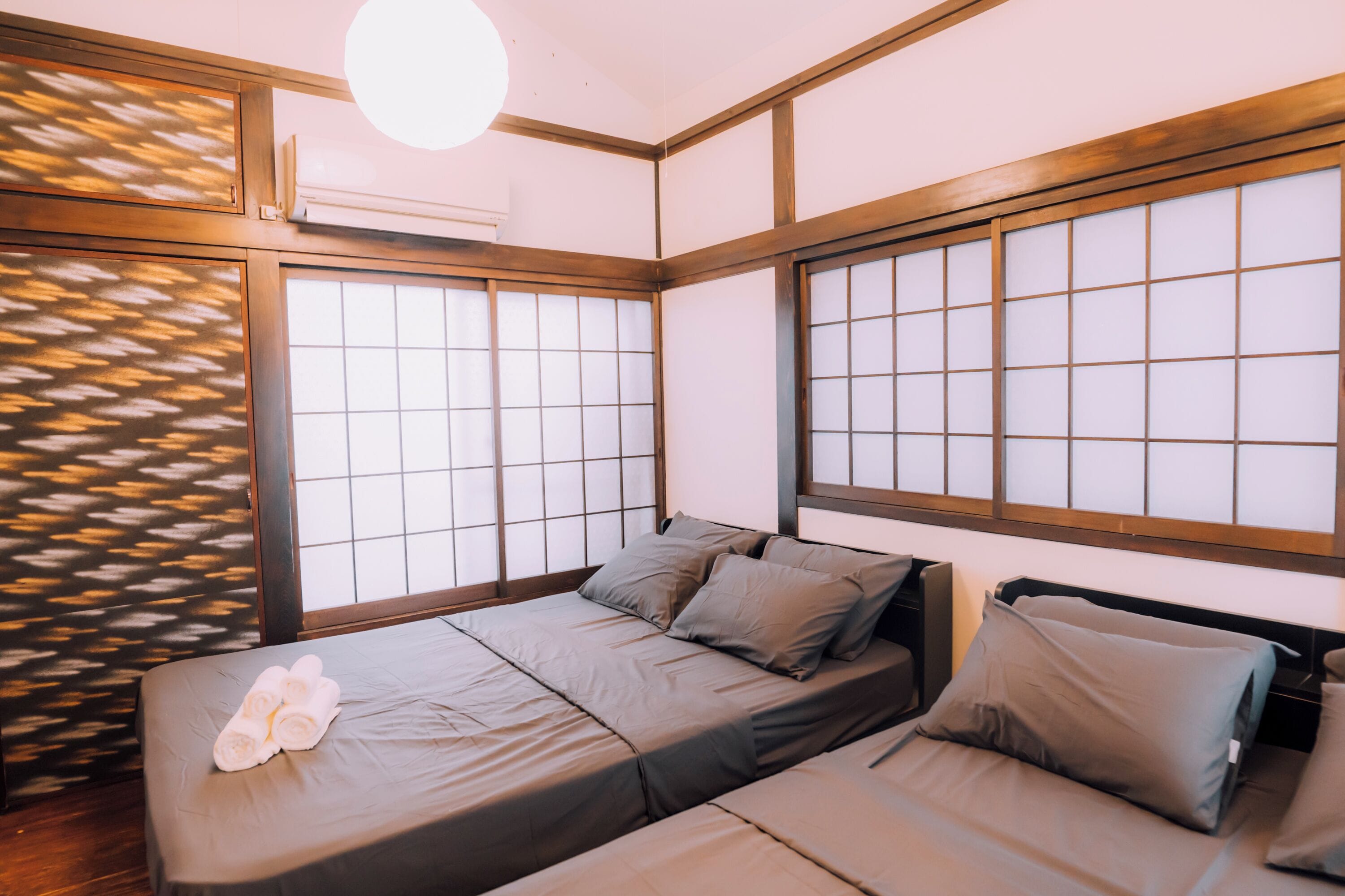 A room with a bed, a window with a grid pattern, and a wall with a wooden frame.