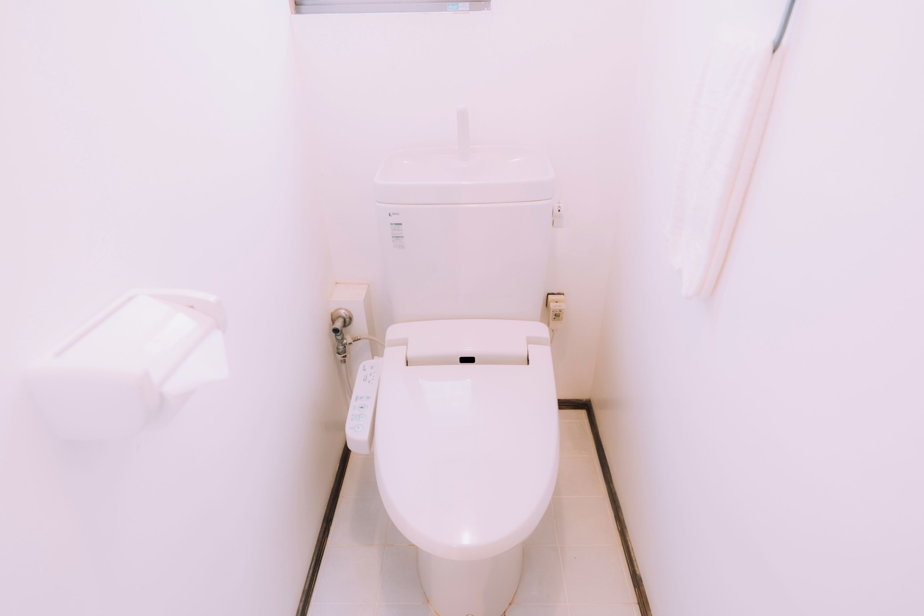 A white toilet with a control panel, a flush handle, and a wall-mounted flush button.