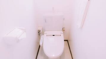 A white toilet with a control panel, a flush handle, and a wall-mounted flush button.