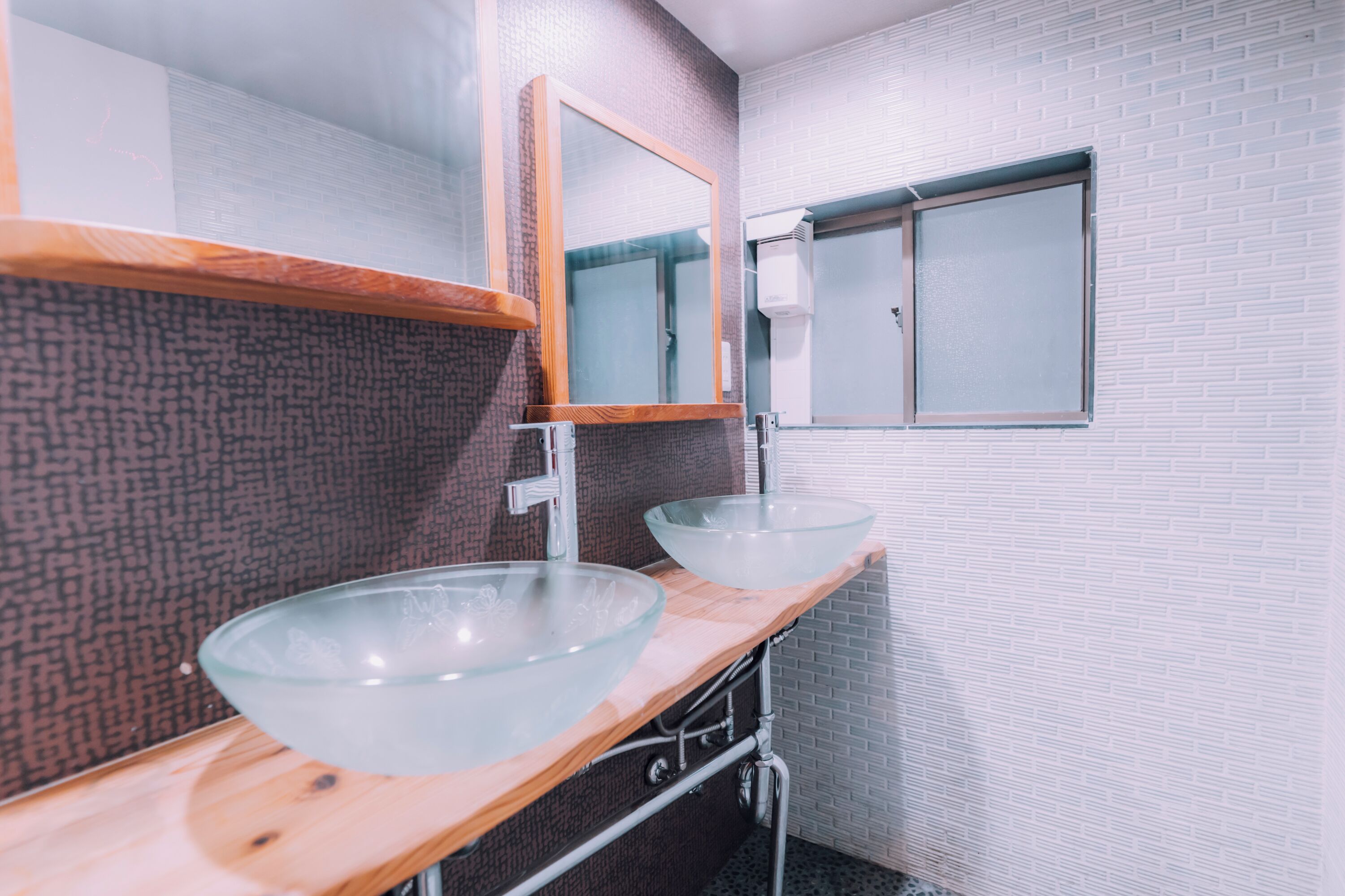 A bathroom with two glass sinks, a wooden countertop, a mirror, and a window.