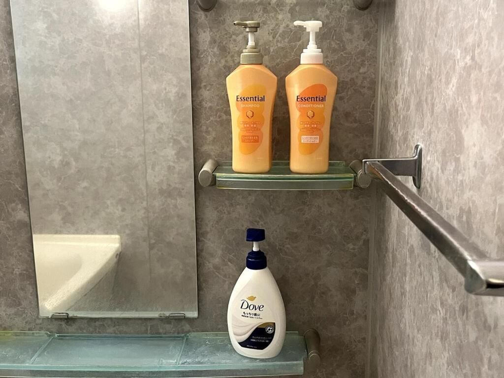 Un baño con un estante de vidrio que contiene dos botellas de champú y acondicionador, y una botella de Dove en un estante inferior.
