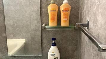 Un baño con un estante de vidrio que contiene dos botellas de champú y acondicionador, y una botella de Dove en un estante inferior.