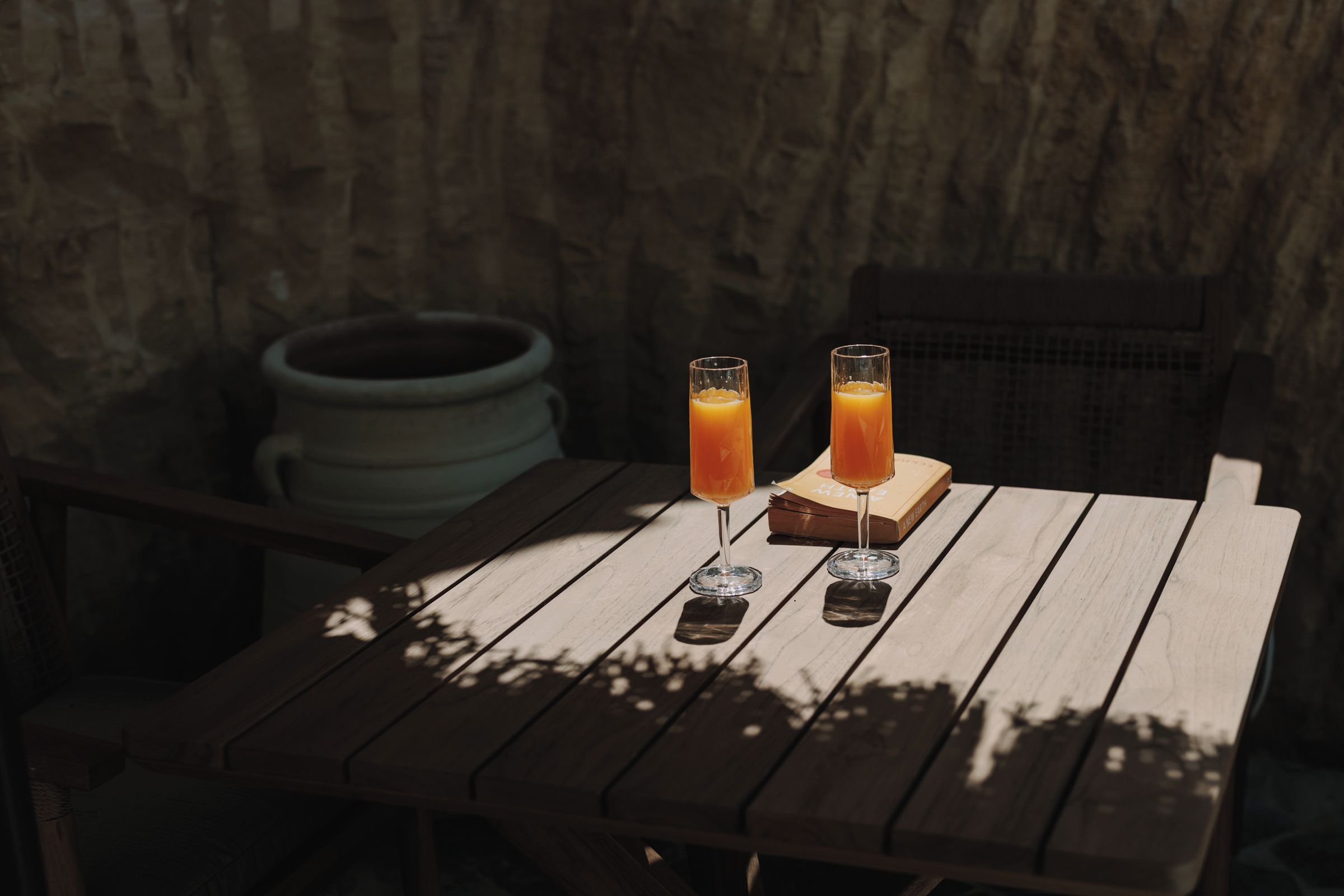 Deux verres de jus d’orange sur une table en bois, avec un mur de briques rustiques en arrière-plan.