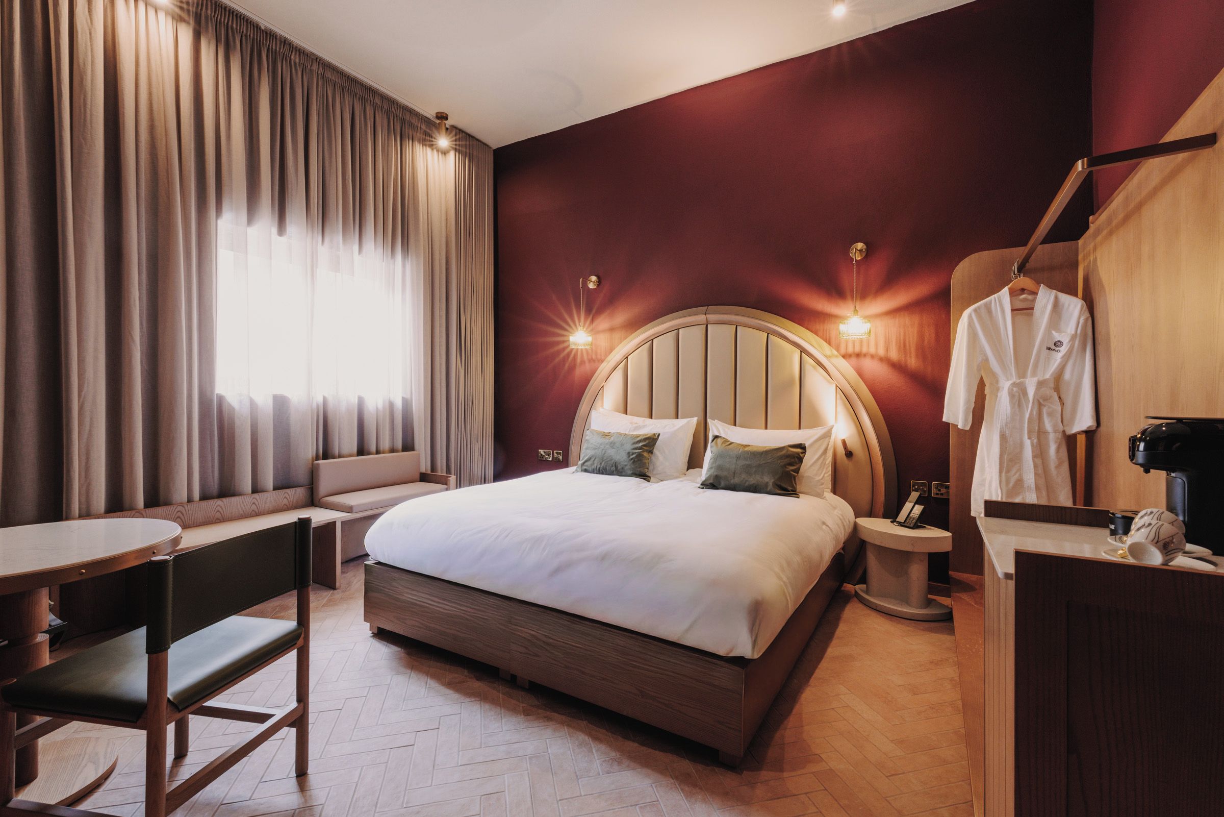 Une chambre d’hôtel avec un grand lit, une table de chevet, une chaise, un bureau, une robe accrochée et une machine à café.