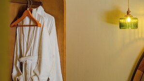 Un albornoz blanco colgado de una percha de madera en una habitación con una puerta de madera y una lámpara colgante verde.