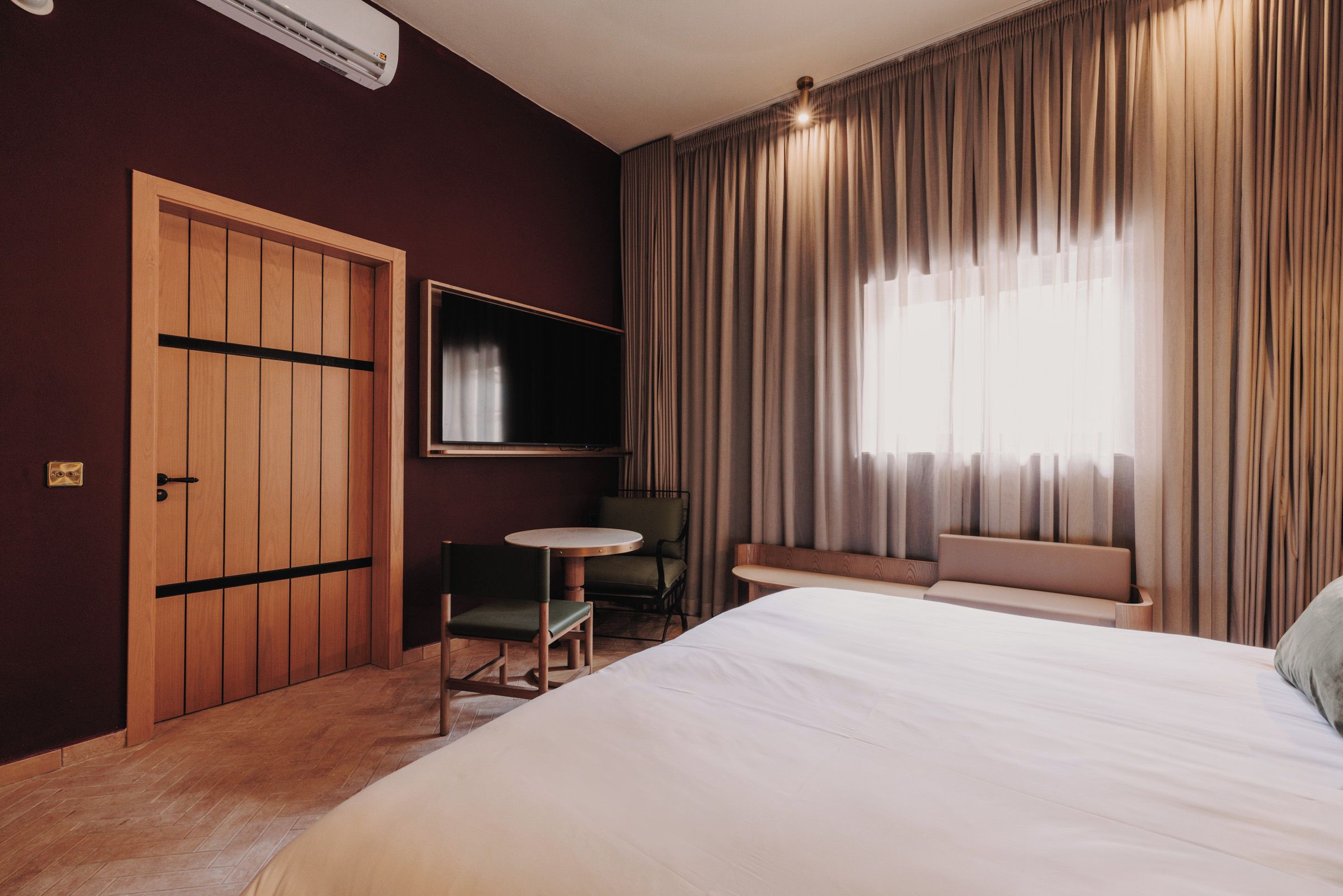 A hotel room with a bed, a desk, a chair, a television, and a window with curtains.