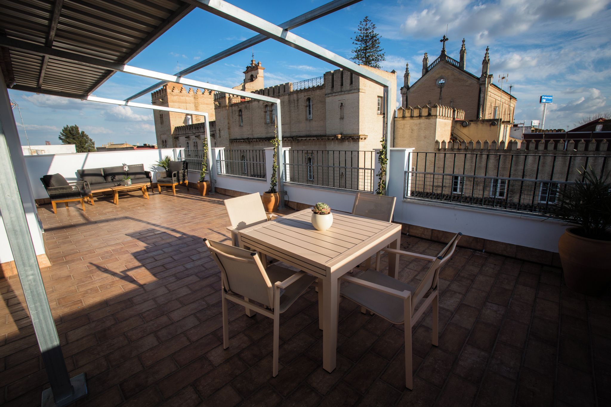 A rooftop terrace with a wooden table and chairs, potted plants, and a view of historic buildings.