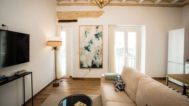 A living room with a flat-screen TV, a floor lamp, a sofa, and a large abstract painting on the wall. - Alijar Casa Boutique (Castilleja de la Cuesta)
