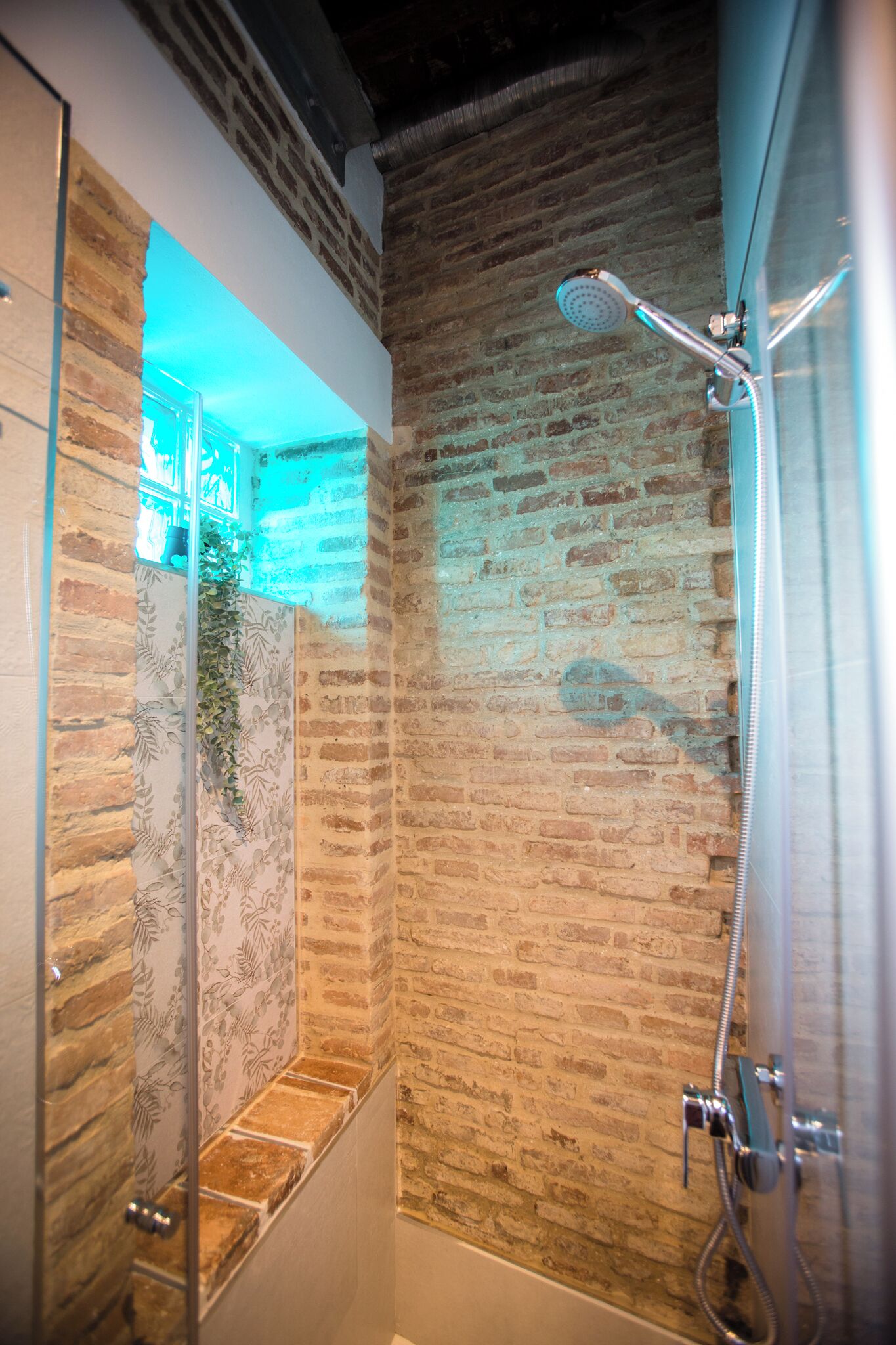 A modern bathroom with a brick wall, a glass shower enclosure, and a visible showerhead.