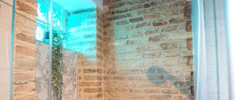 A modern bathroom with a brick wall, a glass shower enclosure, and a visible showerhead.