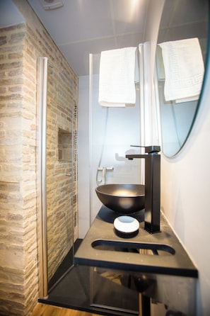 Un bagno con cabina doccia in vetro, un lavandino nero e uno specchio con un asciugamano appeso.