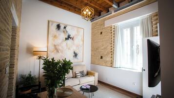 Una sala de estar moderna con un cuadro abstracto grande, techo de madera, pared de ladrillo, un sofá, una mesa de centro y un televisor.