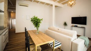 A modern living room with a wooden dining table, a sofa, and a TV mounted on the wall. - Alijar Casa Boutique (Castilleja de la Cuesta)