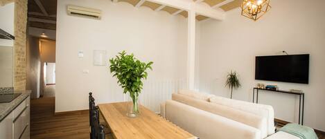 A modern living room with a wooden dining table, a sofa, and a TV mounted on the wall.