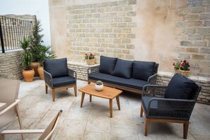 A patio area with wicker furniture, including two chairs, a sofa, and a coffee table. There are potted plants and a basket with flowers. - Alijar Casa Boutique (Castilleja de la Cuesta)