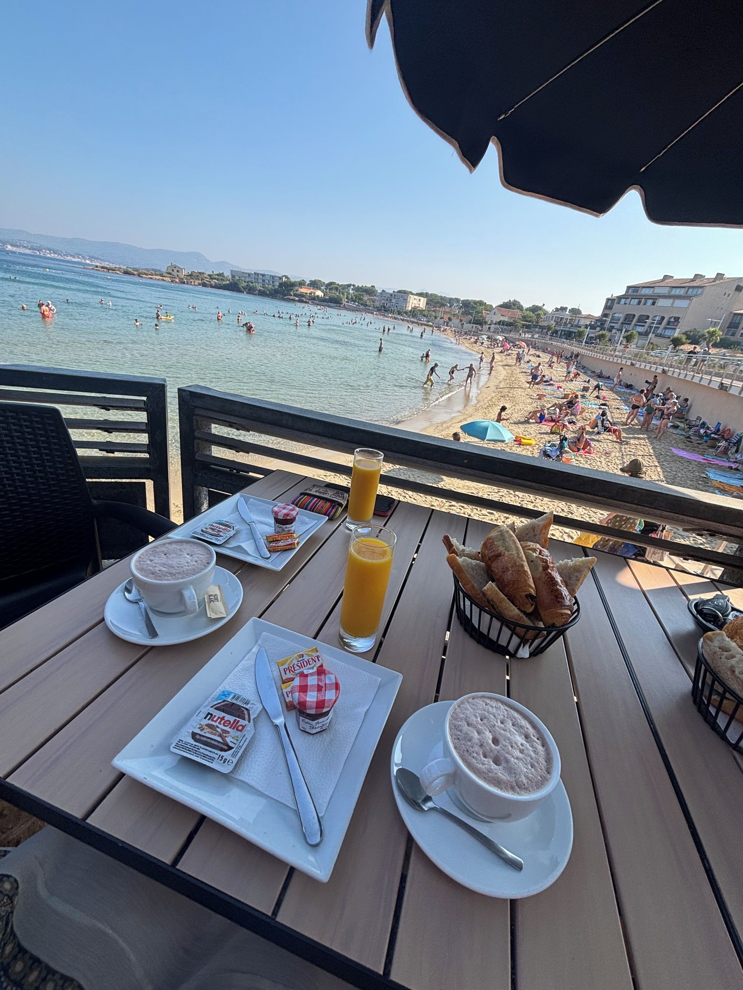 A table with breakfast items and a view of a beach with people swimming and sunbathing.
