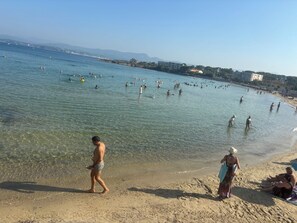 A beach with clear water, people swimming, and buildings in the background. - Villa le Soleil Du Brusc, just 7 minutes from Le Brusc Beach! (Six-Fours-les-Plages)