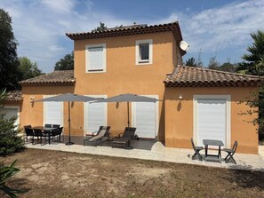 Ein zweistöckiges Gebäude mit einer Terrassenfläche, komplett mit Tisch, Stühlen, Liegen und Sonnenschirmen.