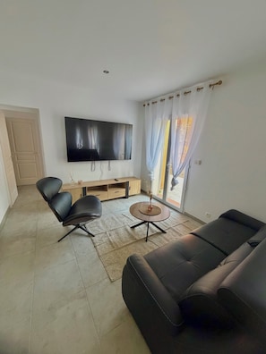 A living room with a flat-screen TV, two black leather sofas, a wooden coffee table, and a sliding glass door with curtains. - Villa le Soleil Du Brusc, just 7 minutes from Le Brusc Beach! (Six-Fours-les-Plages)