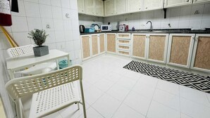 Cocina compacta con armarios blancos, un lavamanos y una zona de comedor con una silla y una mesa.