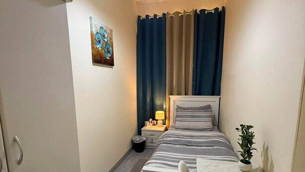 Habitación de hotel pequeña con cama, escritorio, silla, mesita, planta en maceta, un cuadro en la pared y una lámpara colgante.