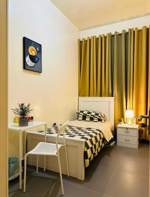Un dormitorio pequeño y ordenado con cama, mesita de noche, silla y escritorio con una planta.