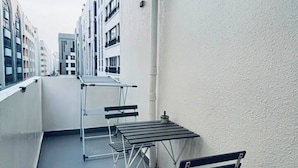 Un balcón con mesa y sillas, un tendedero y vista a edificios al fondo.