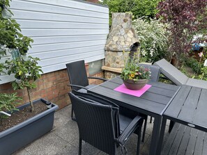 An outdoor patio with a table and chairs, a potted plant, and a stone feature.