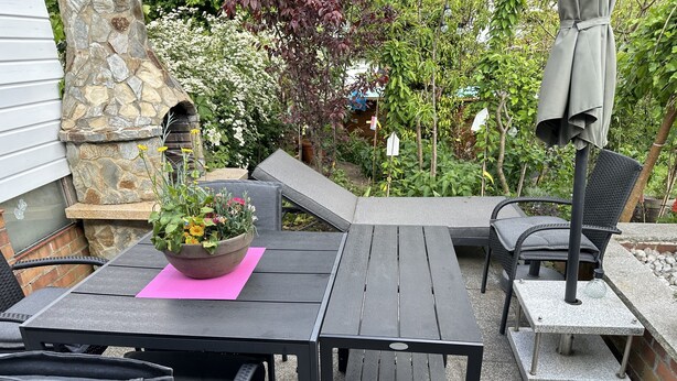 Une terrasse extérieure avec un mur en pierre, une table en bois et des chaises en osier noir.