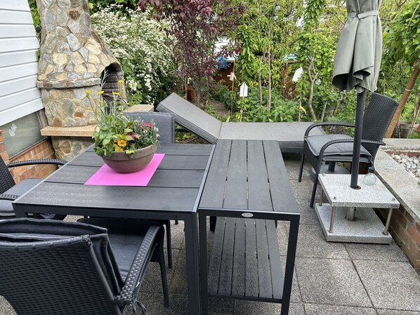 An outdoor patio with a stone wall, a wooden table, and black wicker chairs.