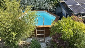 Une piscine entourée d’une végétation luxuriante, dotée d’une terrasse en bois et d’un ensemble de panneaux solaires.