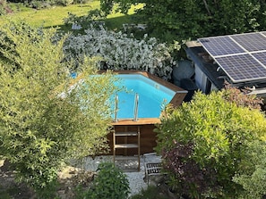 A swimming pool surrounded by lush greenery, with a wooden deck and a solar panel array.