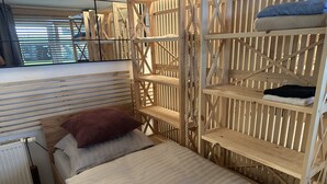 Une pièce comprenant un lit, une étagère en bois et une fenêtre avec des stores.