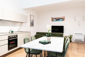 Een moderne keuken met witte kasten, een inbouwoven en een eethoek met een witte tafel en groene stoelen.