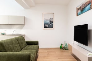 Een moderne woonkamer met een groene bank, een flatscreen-tv en een lijst met een foto van een kustlandschap.