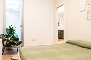 Een kamer met een bed, een stoel, een plant en een deur naar een andere kamer.