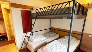 A bunk bed room with two beds, a ladder, a red door, and a wooden bench.