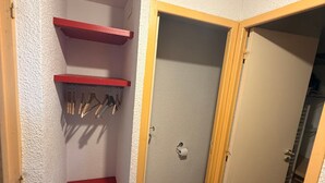A corner room with a red shelf, a door, and a wooden floor.