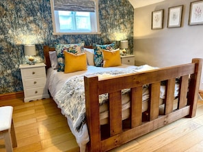 A bedroom with a wooden bed frame, floral-patterned bedding, and a nightstand with a lamp. - The Old Ropery at Mill Cottage  (Ollerton)