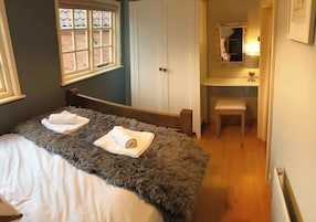Un dormitorio con cama, ventana, armario, espejo y mesita de noche.